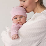 Baby iført lyserød hue holdt i favn af voksen
