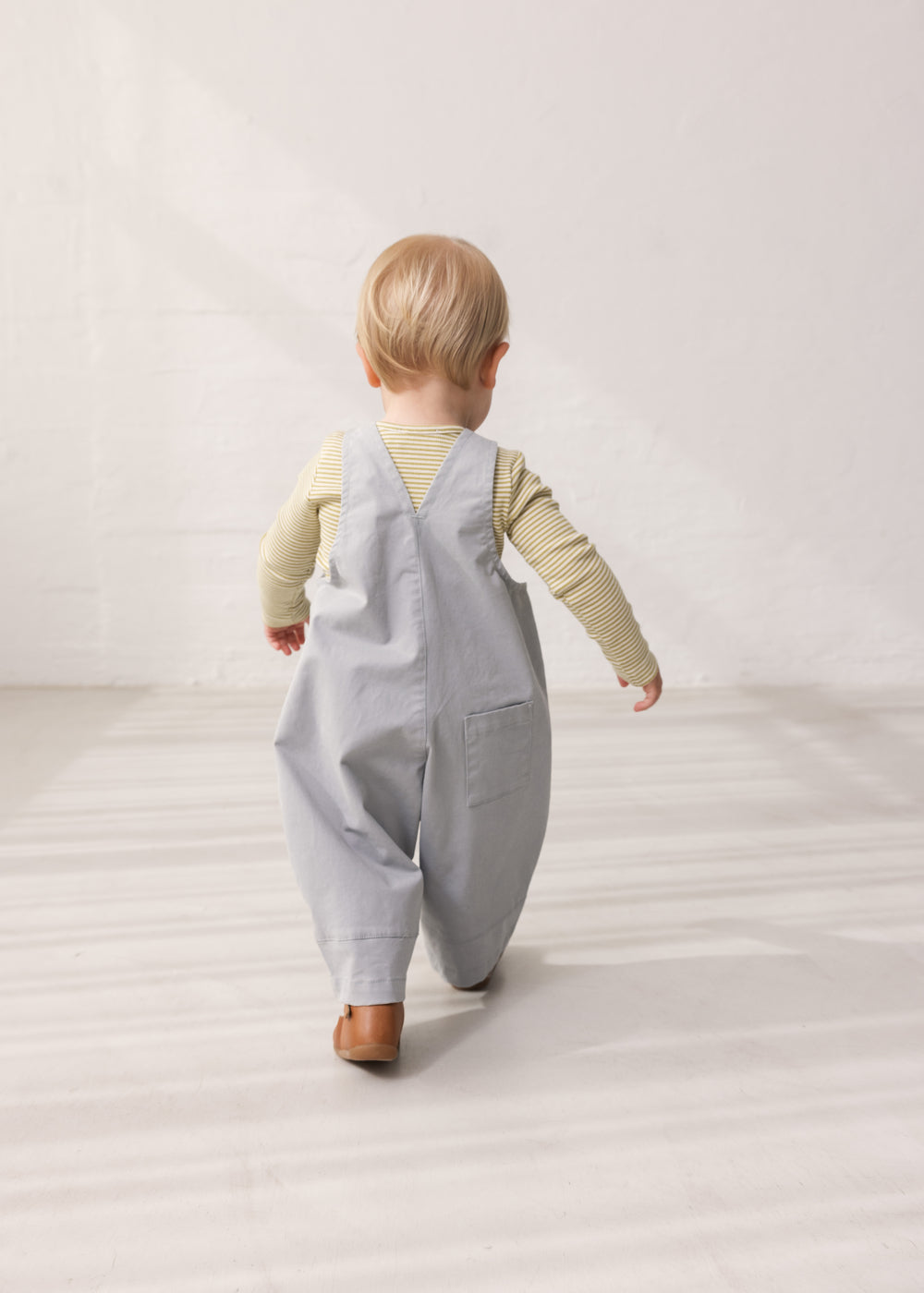 Barn iført grønstribet body under grå overalls