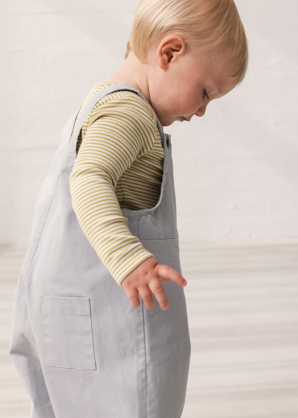 Barn iført grønstribet body under grå overalls