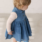 Barn iført blå denimkjole med knapper og langærmet lyserød body