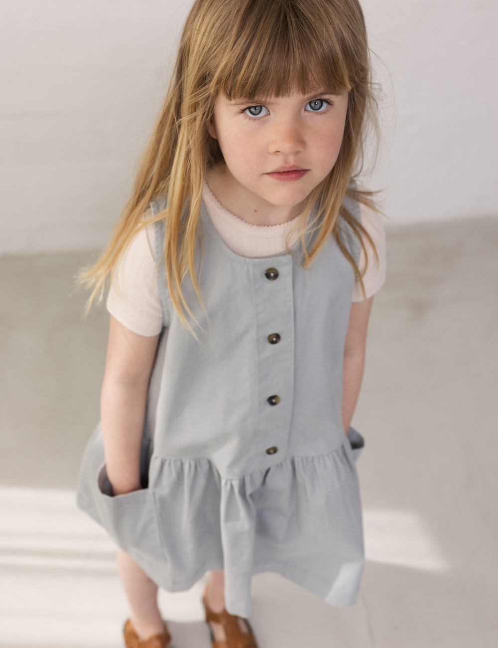 Barn iført grå kjole uden ærmer med knapper og lommer
