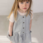 Pige iført ærmeløs blå chino kjole med knapper og lyserød t-shirt