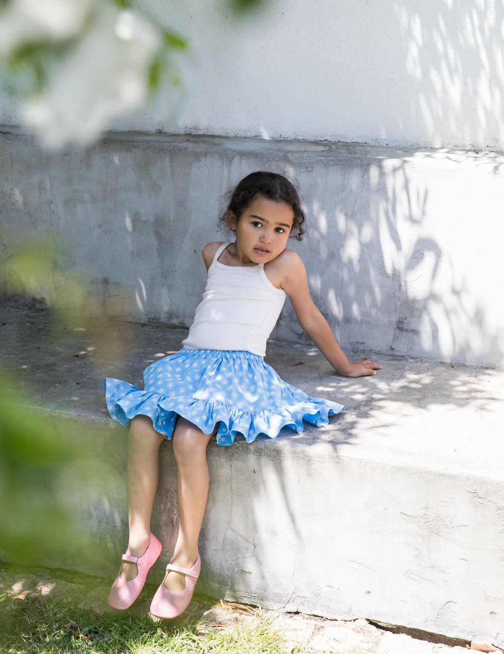 Pige iført hvid top og blå nederdel med små blomsterprint samt lyserøde sko