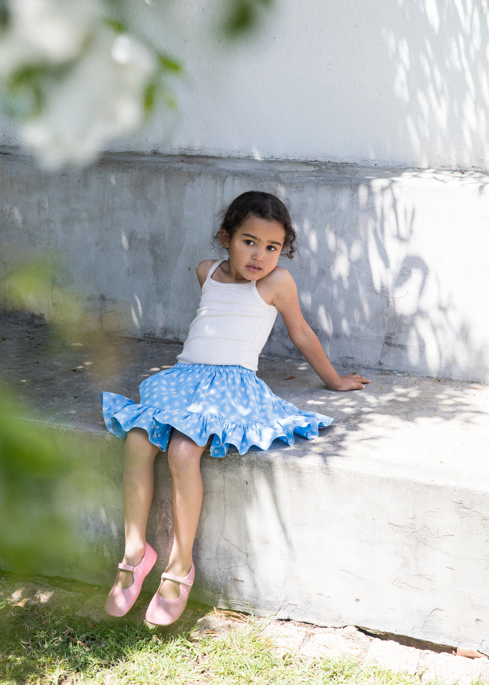 Pige iført hvid top og blå nederdel med små blomsterprint samt lyserøde sko