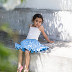 Pige iført hvid top og blå nederdel med små blomsterprint samt lyserøde sko