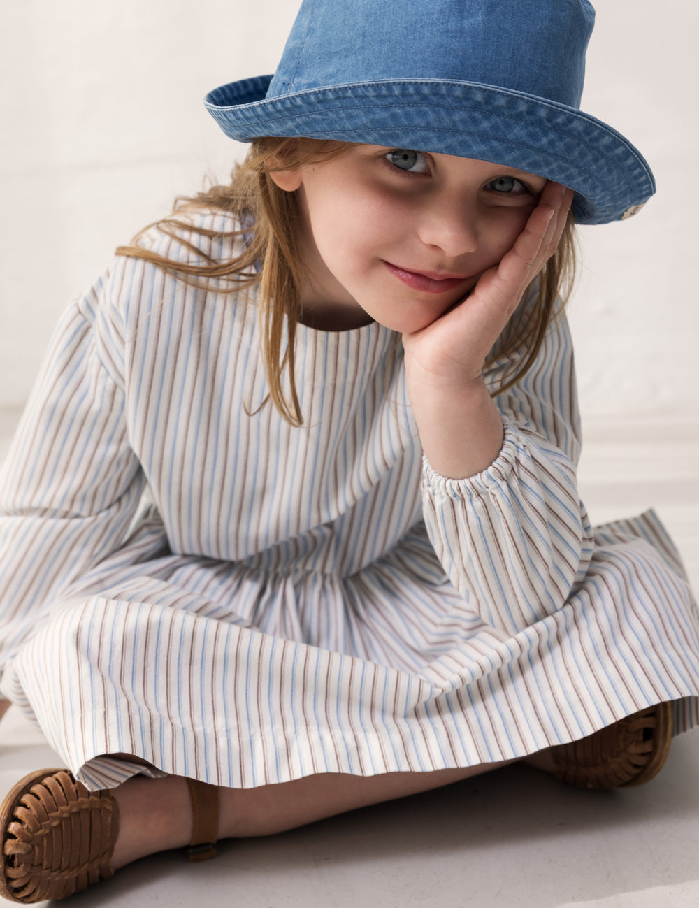 Barn iført blå bøllehat og stribet kjole