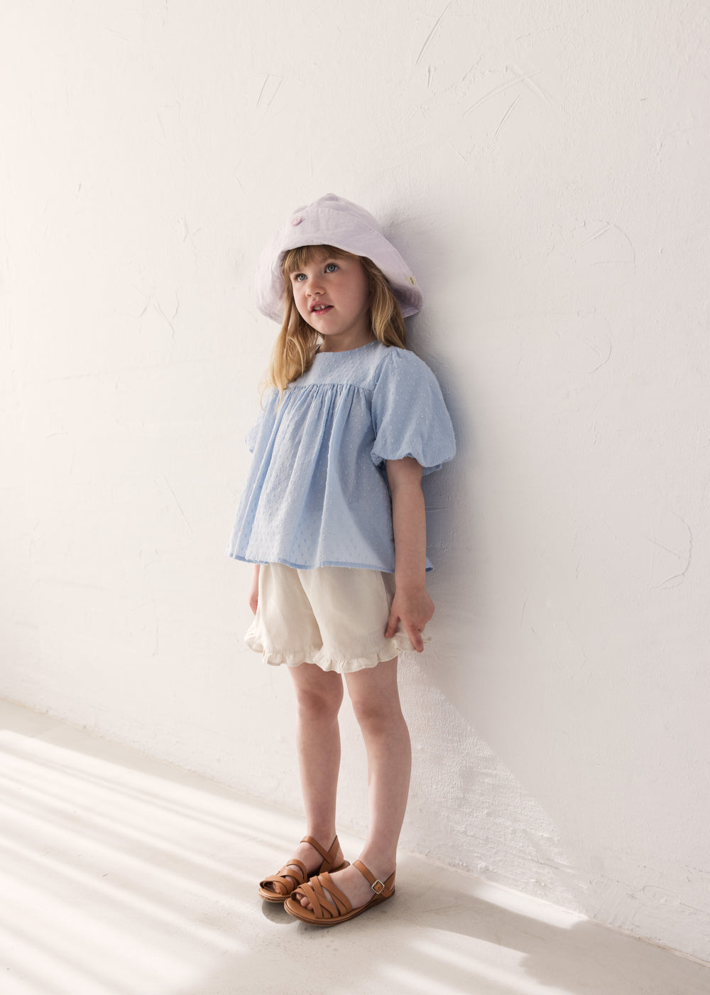Barn iført lys blå top, lyse shorts og sommerhat