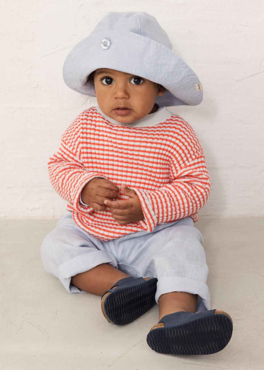 Baby iført Lyseblå bukser, stribet bluse og solhat 