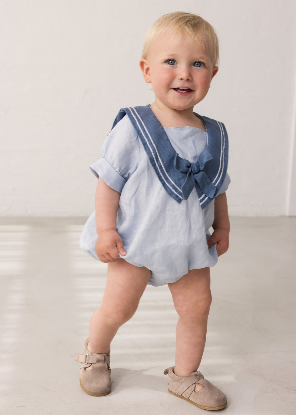 Bay iført kortærmet heldragt med matroskrave og dekorativ sløjfe