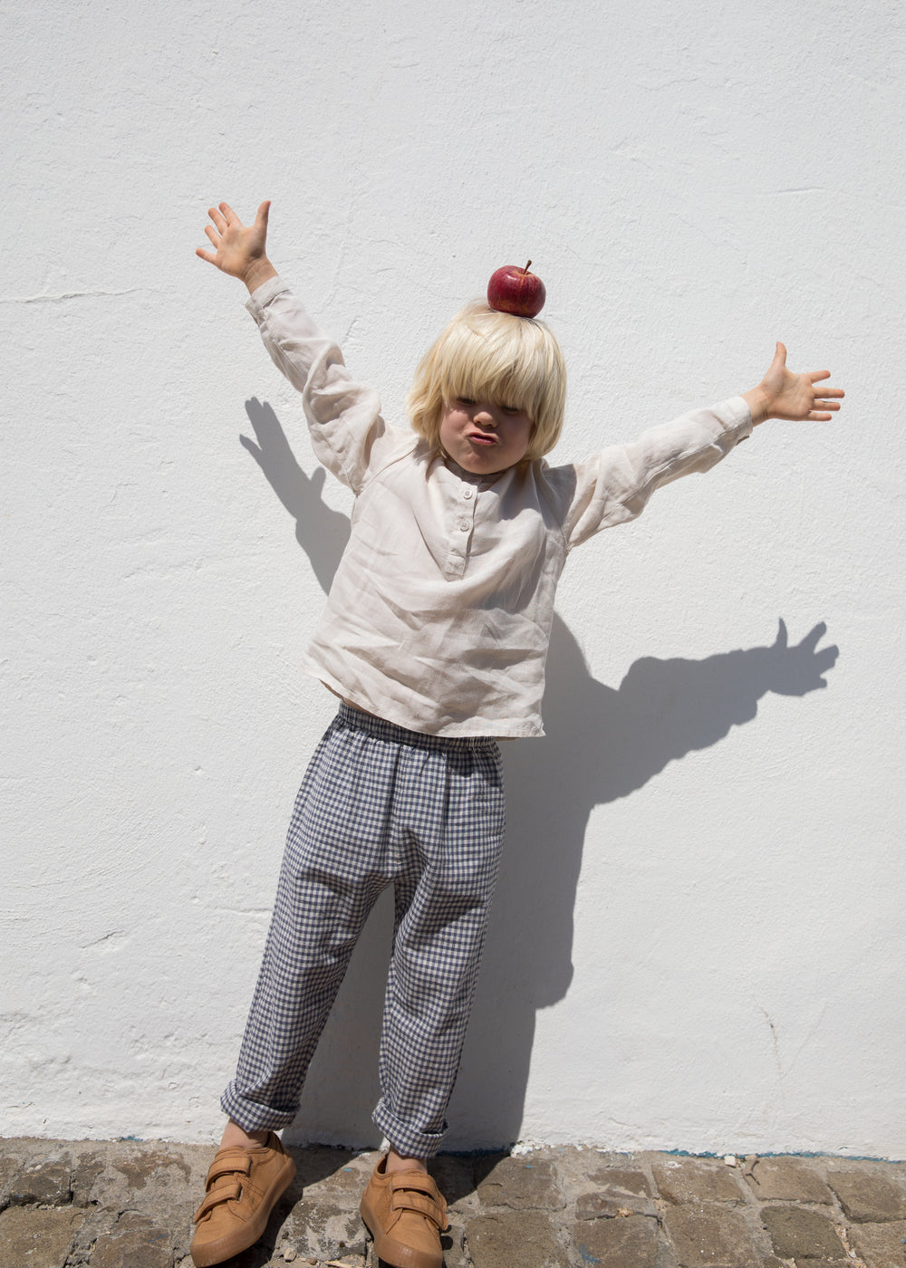 Barn iført lys trøje og ternet bukser med armene løftet