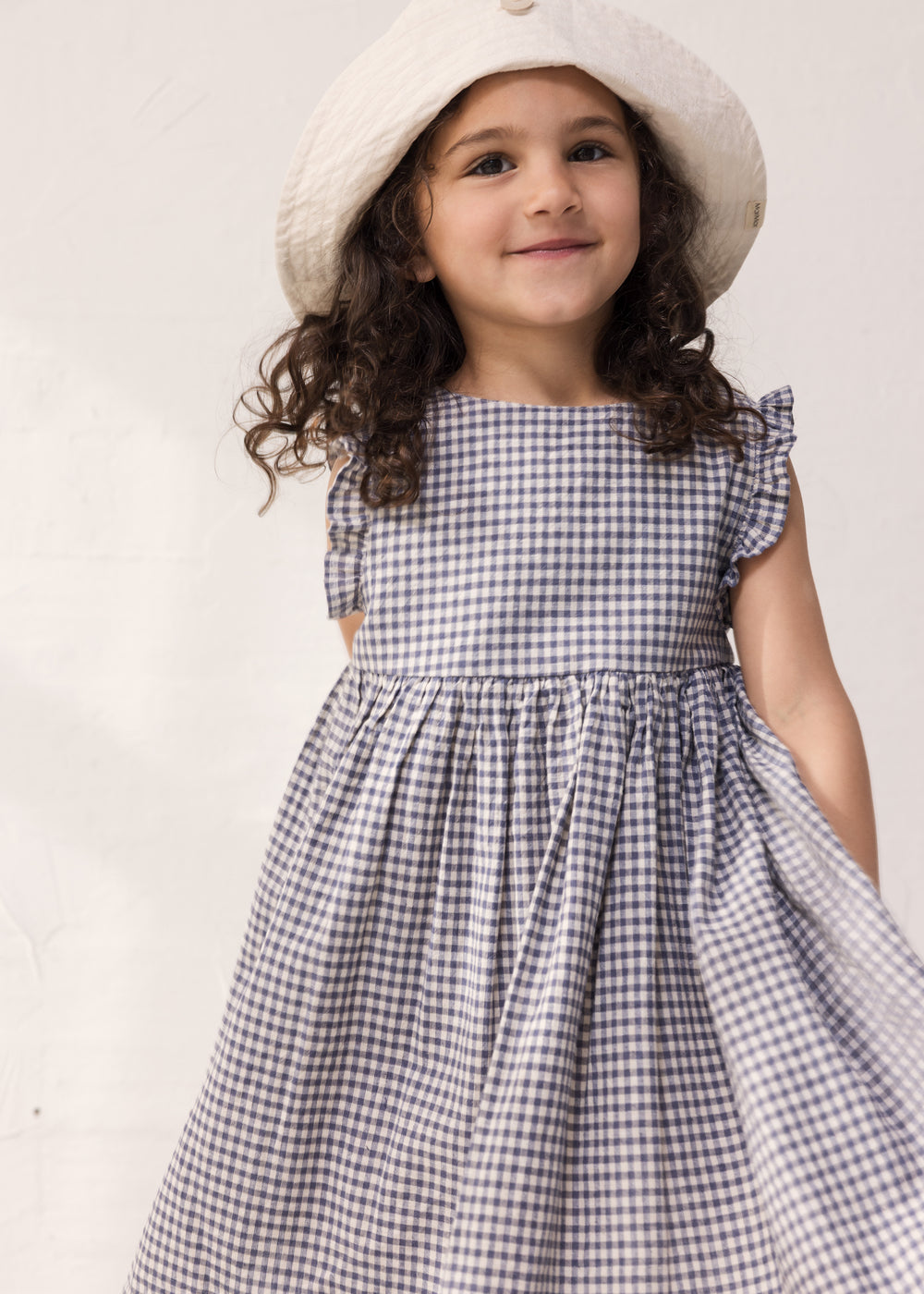 Barn iført ternet kjole med flæser og sommerhat