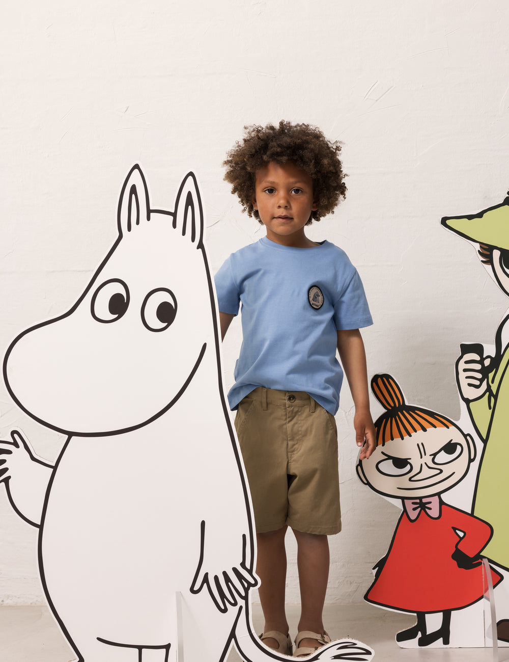 Barn iført lyseblå T-shirt og khakifarvede shorts sammen med Moomin figurer
