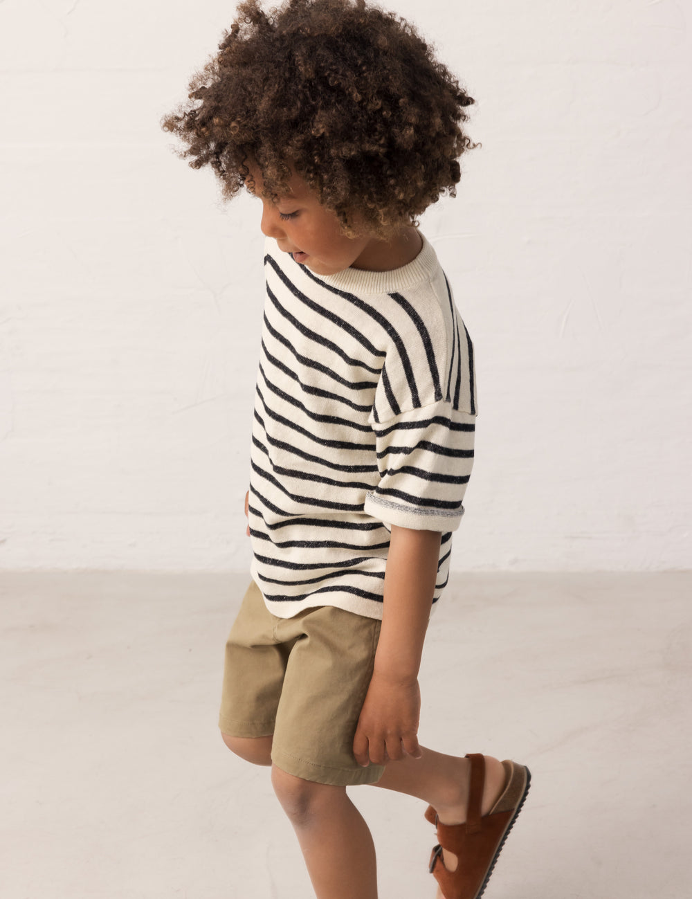 Barn iført stribet bluse og grønne shorts set fra siden