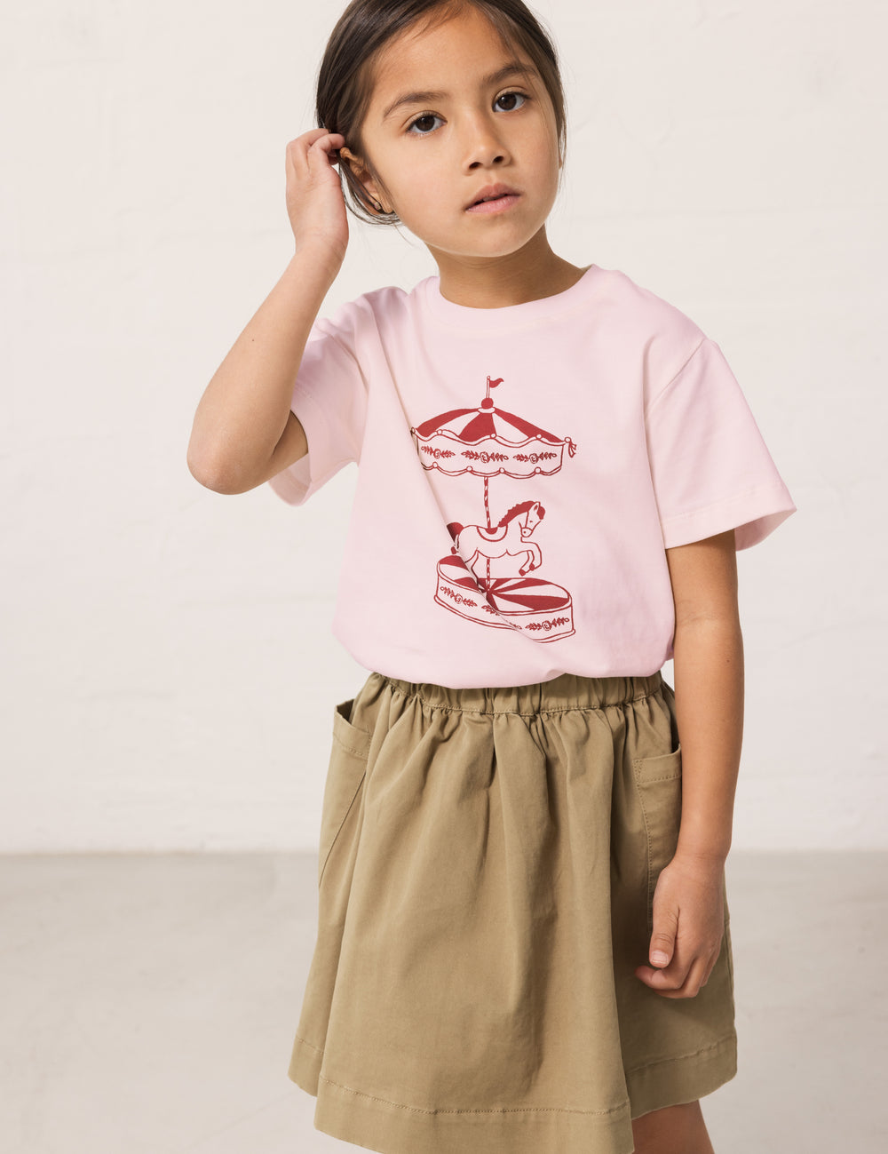 Pige iført grøn chino nederdel og lyserød t-shirt