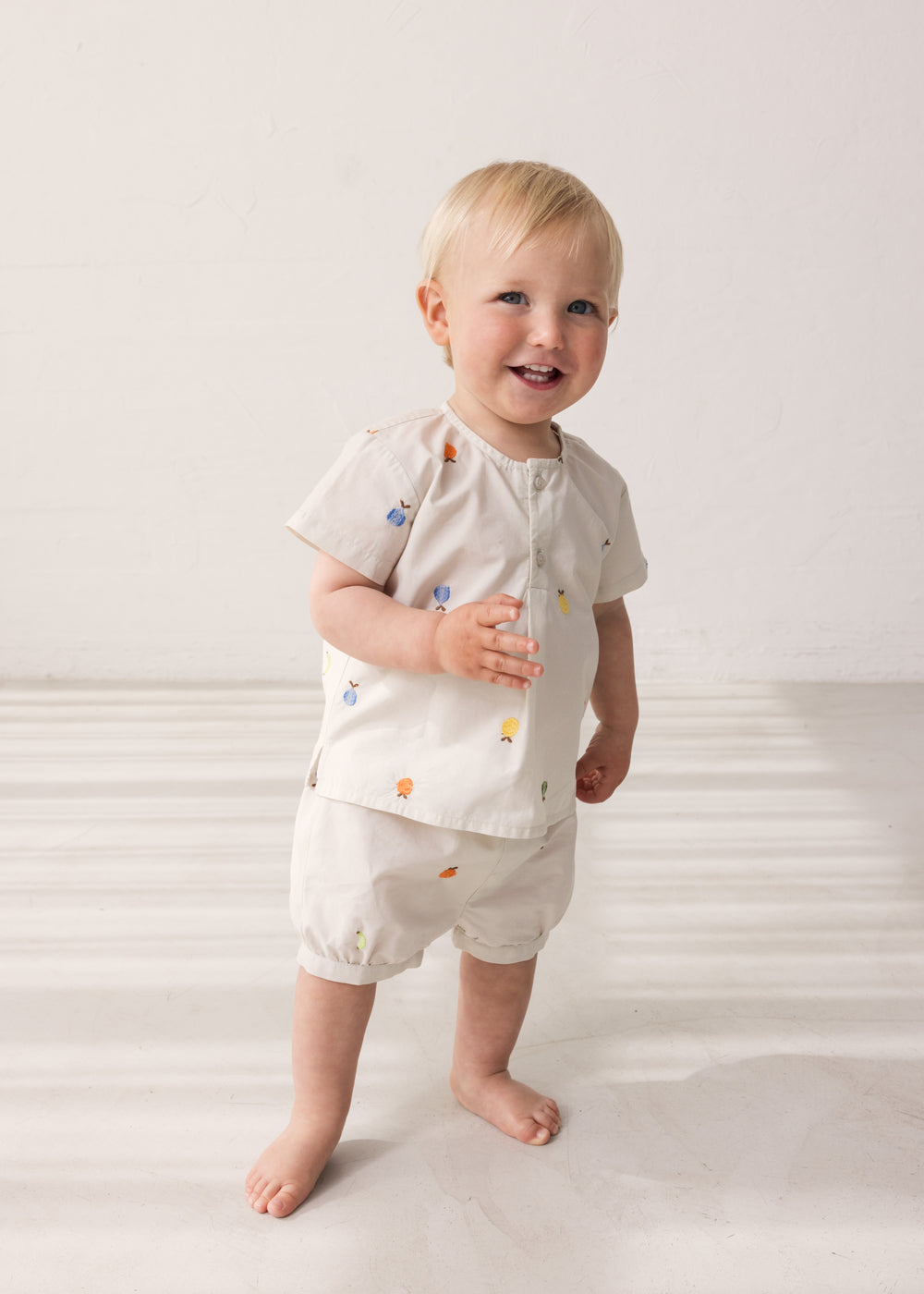 Baby iført lys T-shirt og bloomers med frugtbroderi