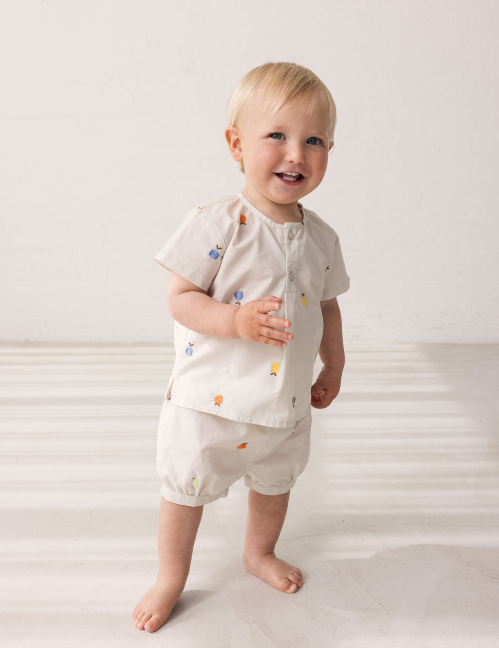 Baby iført lyse shorts med broderede frugter og matchende bluse