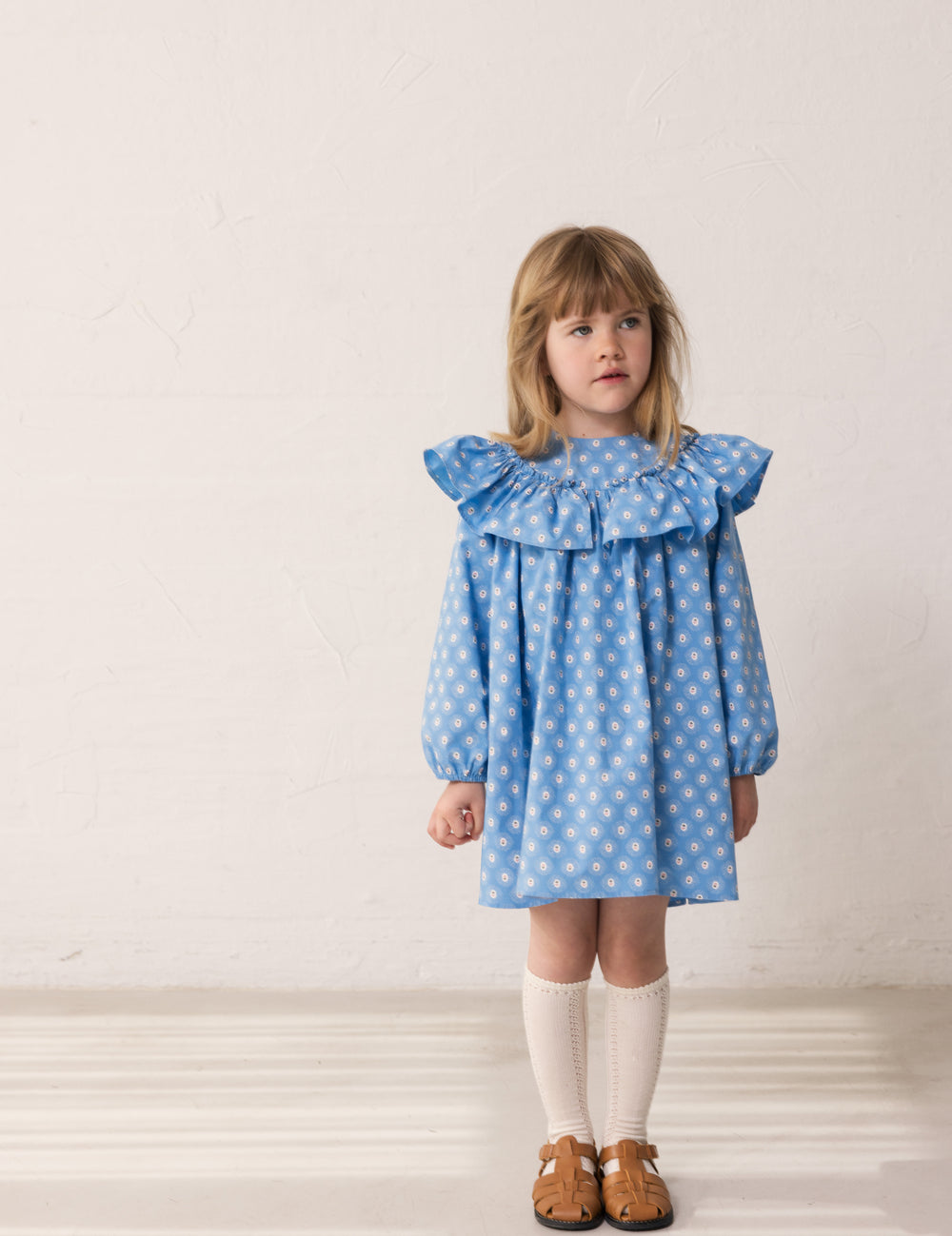 Barn iført blå kjole med blomsterprint og flæsedetalje