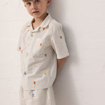 Barn iført skjorte og shorts med frugtbroderi