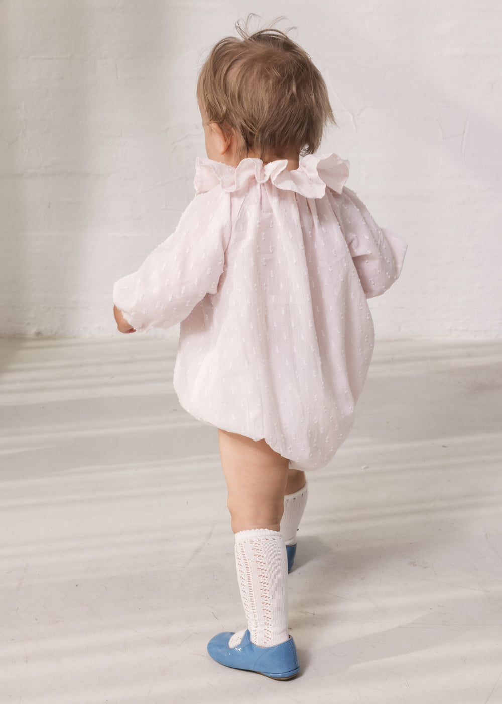 Baby iført lyserød heldragt med lange ærmer og flæsekrave