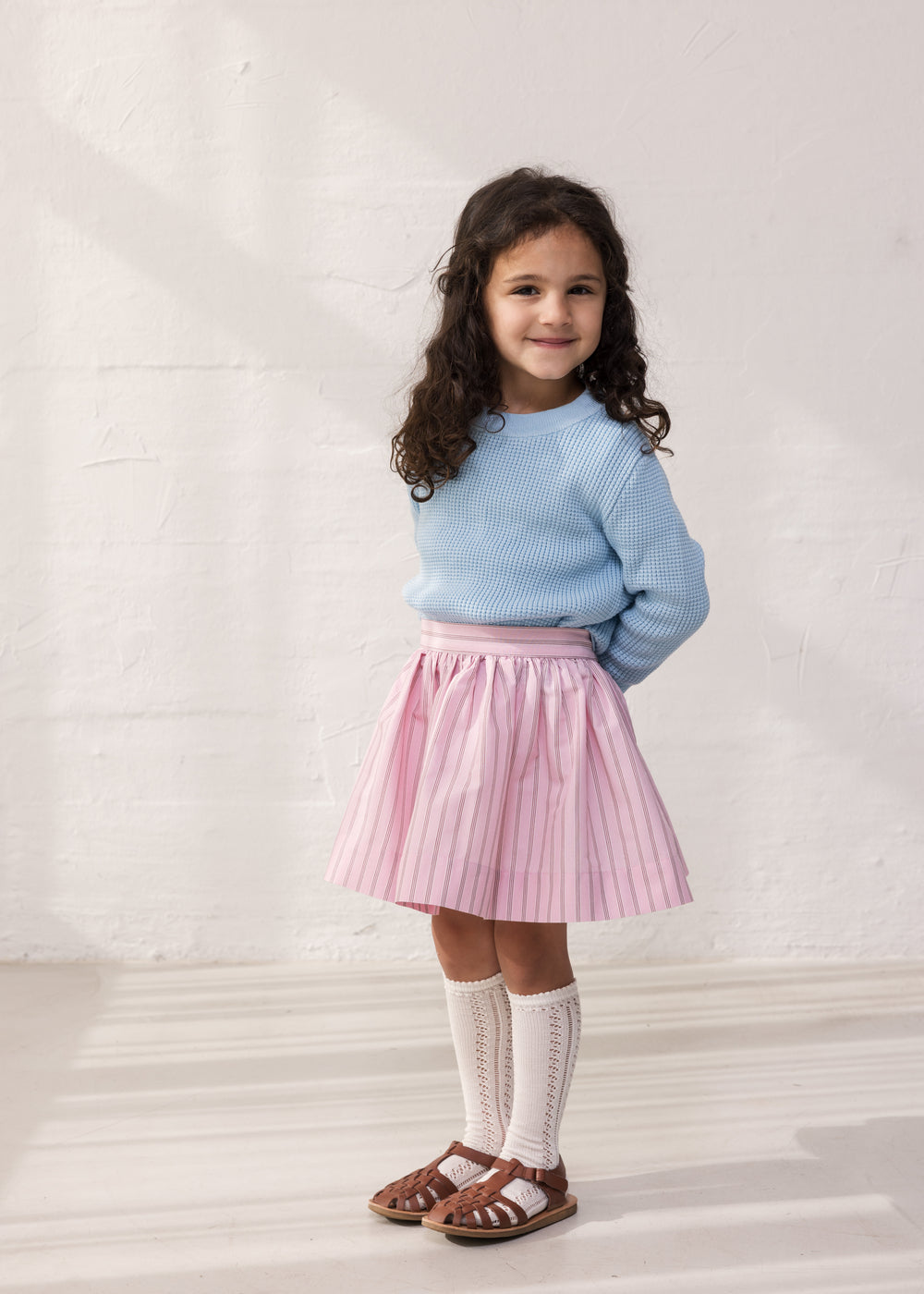Pige iført blå striktrøje og lyserød nederdel
