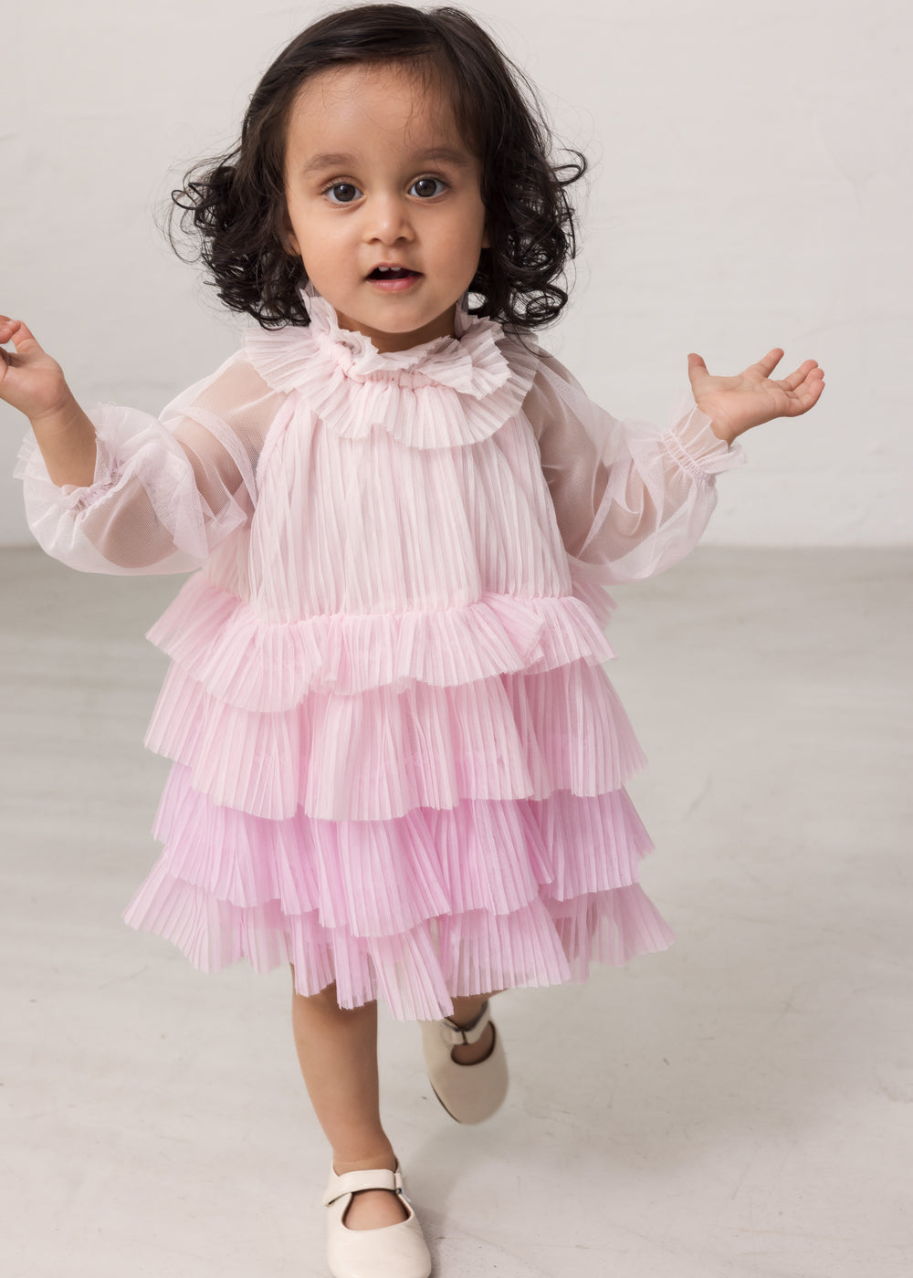 Pige iført lyserød langærmet baby kjole i plisseret tyl med flere lag