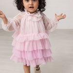 Pige iført lyserød langærmet baby kjole i plisseret tyl med flere lag