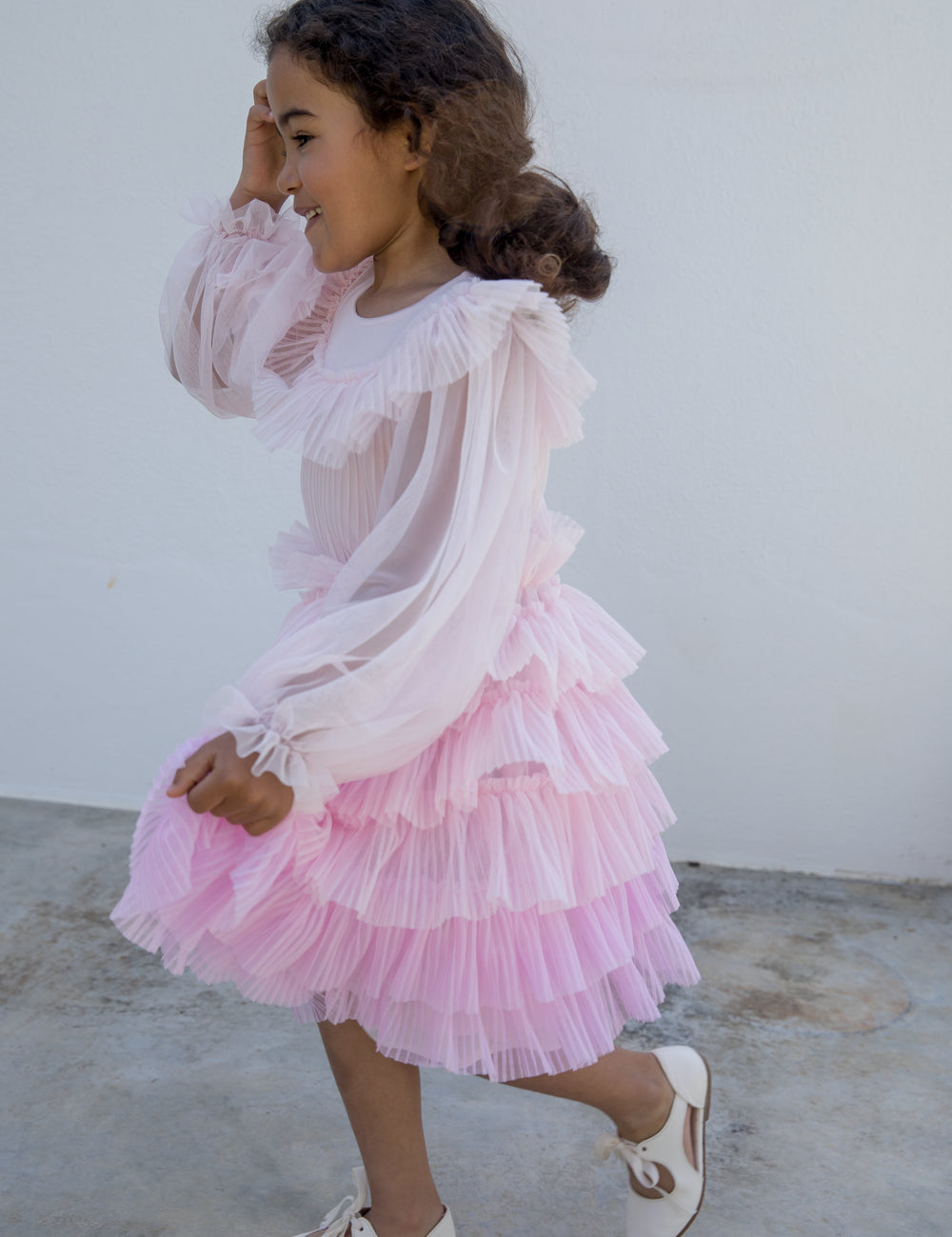 Pige iført lyserød langærmet kjole i plisseret tyl med flere lag