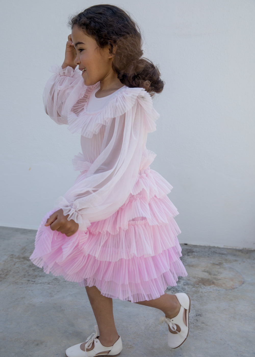 Pige iført lyserød langærmet kjole i plisseret tyl med flere lag