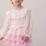 Pige iført lyserød langærmet kjole i plisseret tyl med flere lag