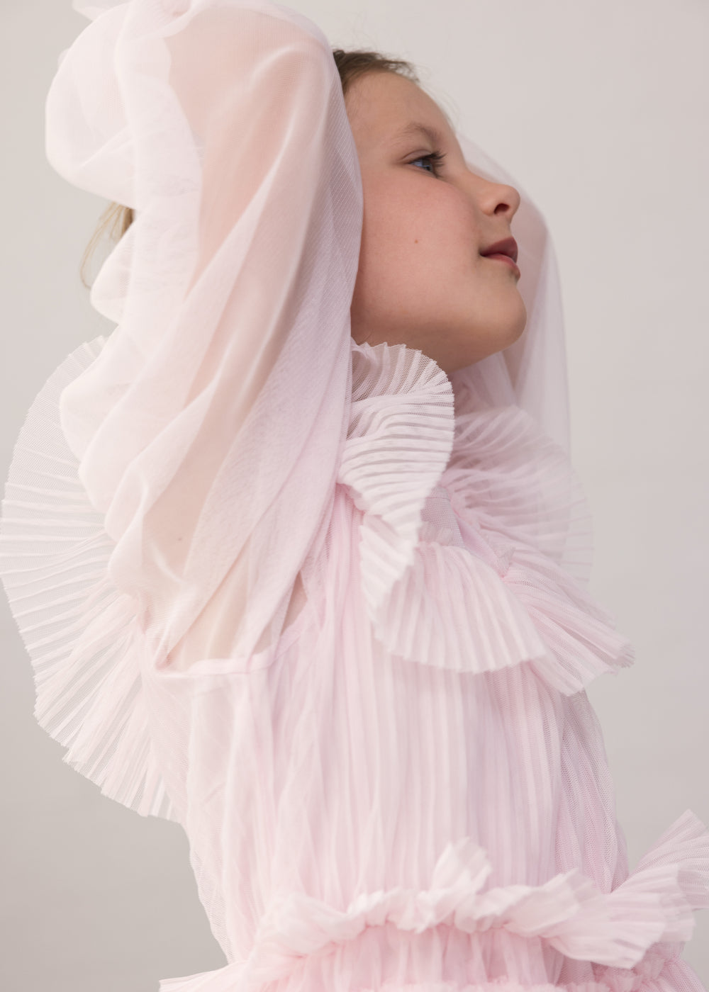 Pige iført lyserød langærmet kjole i plisseret tyl med flere lag
