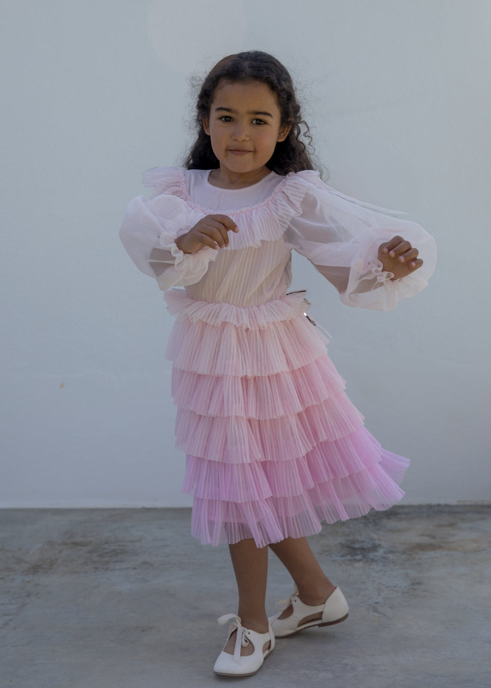 Pige iført lyserød langærmet kjole i plisseret tyl med flere lag