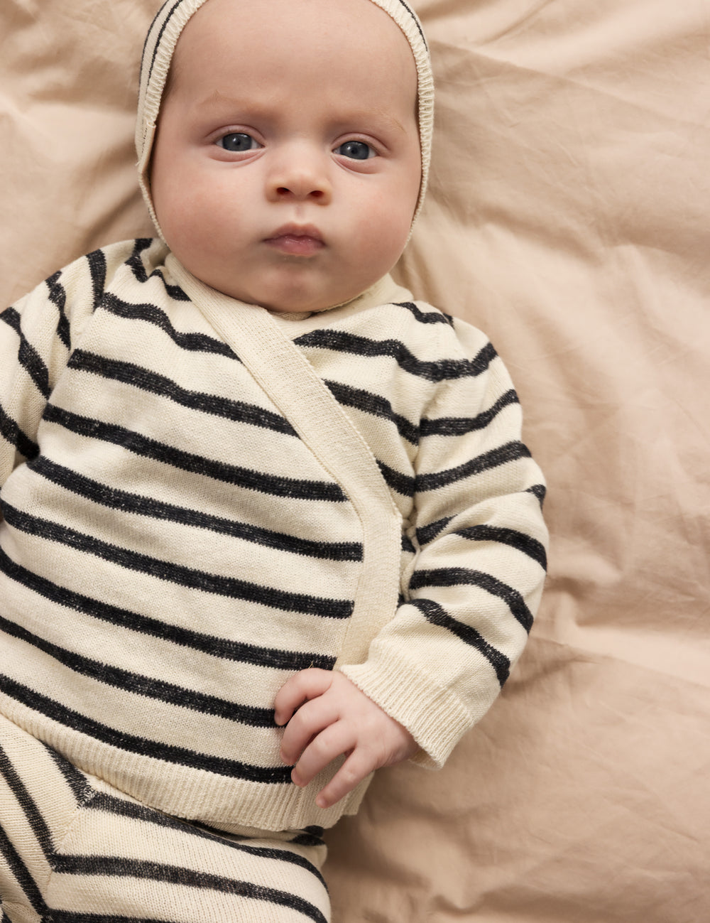 Baby iført strik cardigan med striber og slå-om lukning, matchende bukser og hue