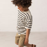 Barn iført stribet bluse og grøne shorts set fra siden