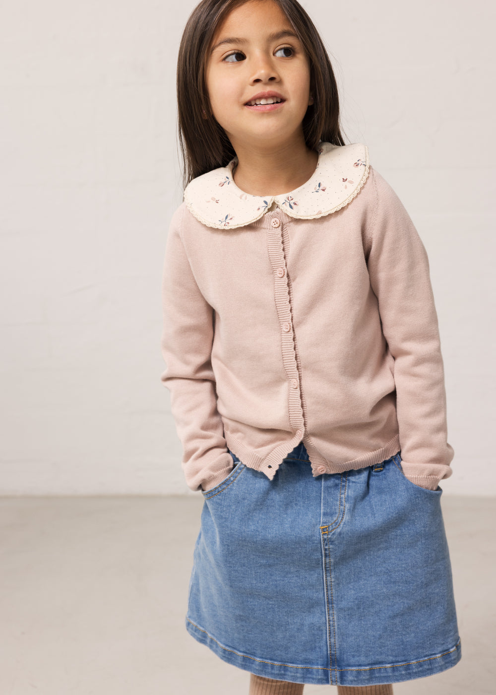 Barn iført lyserød cardigan med krave og denimnederdel