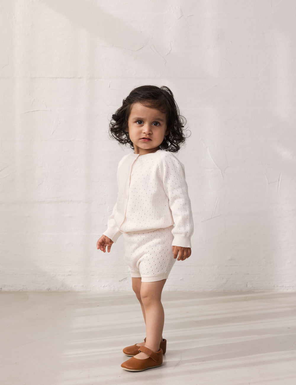 Pige iført strik cardigan med fint hulmønster og knaplukning og matchende shorts