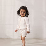 Pige iført strik cardigan med fint hulmønster og knaplukning og matchende shorts