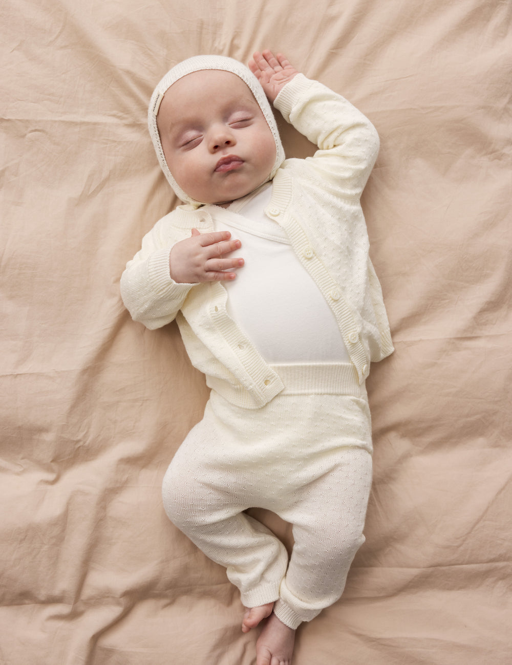 Baby iført råhvid heldragt og matchende babyhjelm