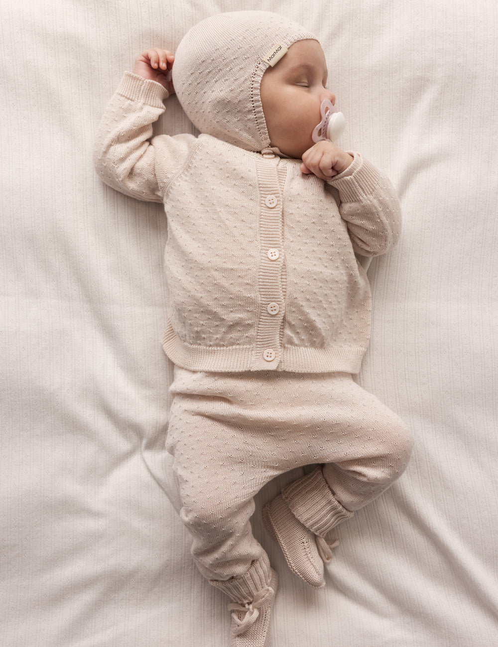 Baby iført lyserødt strikket sæt med bukser og hue