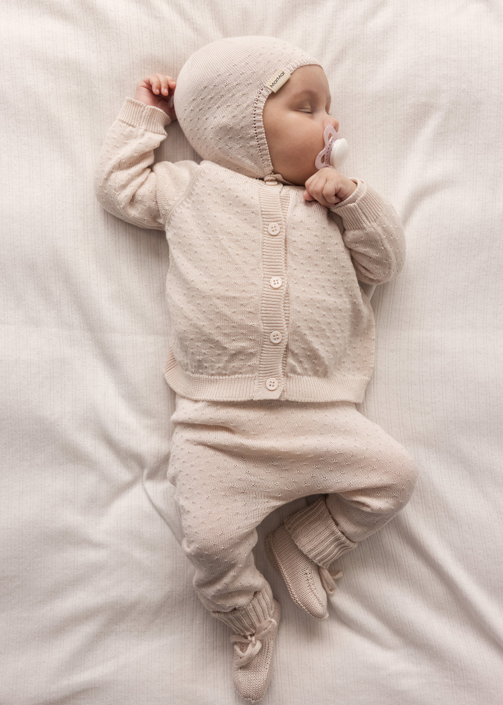 Baby iført lyserød cardigan, bukser og babyhue