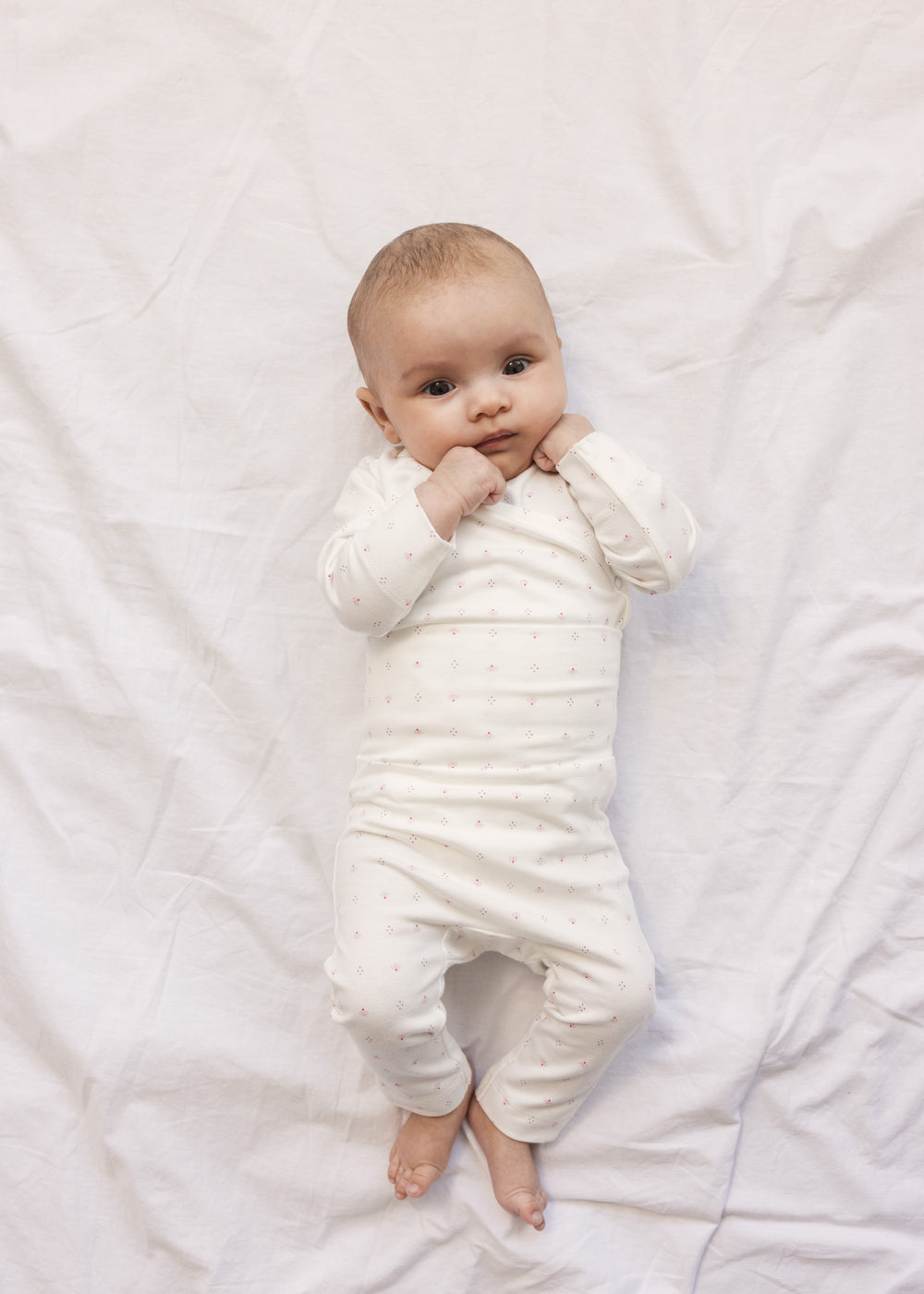 Baby i hvid baby bodystocking og bukser med små blomster