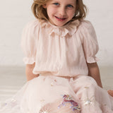 Pige der sidder i en lyserød tyl nederdel  med enhjørninger og stjerner og en lyserød bluse med krave