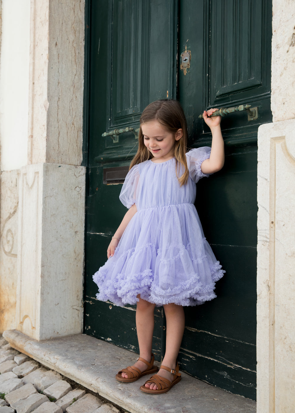 Pige der står i en lyselilla tylkjole foran en grøn dør