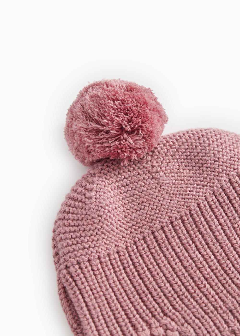 Strikhue i rosa-lilla med stor pompon og ensartet strikmønster