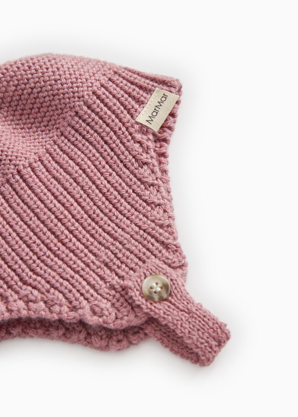 Detalje af strikhue i rosa-lilla: ribstrik, mærkat og lille knap