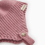 Detalje af strikhue i rosa-lilla: ribstrik, mærkat og lille knap