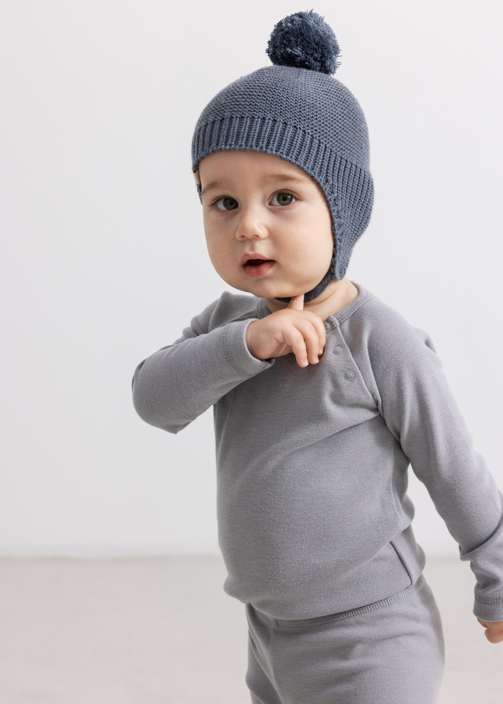 Grå strikhue med pompom, ribbet kant og ørelomme