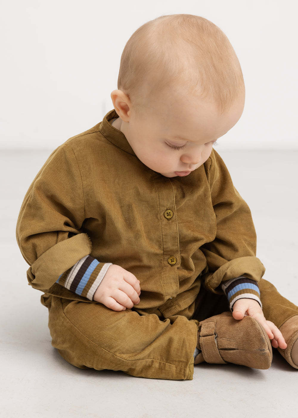 Baby set forfra i brun heldragt med stribede manchetter og ribkant ved ærmer.