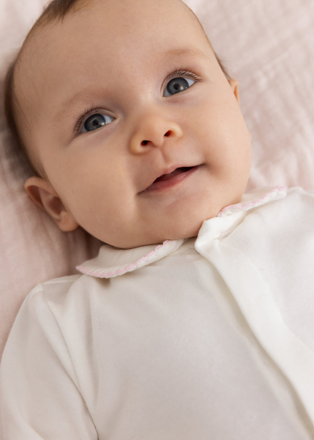 Baby i off-white heldragt med lyserød kant ved hals og knapdetalje