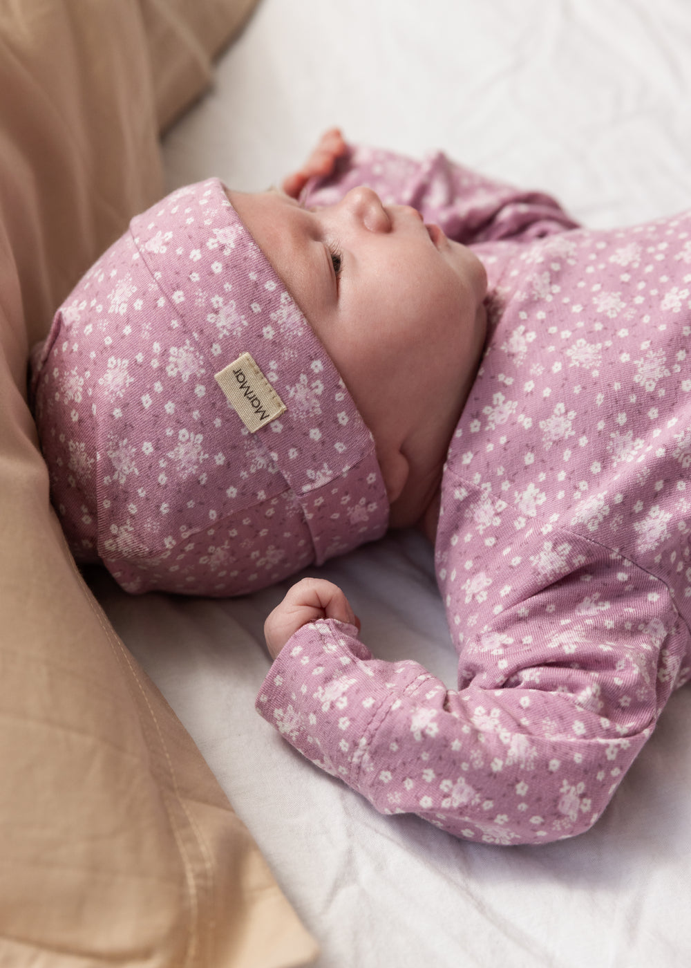 Baby iført lyserød hue med små hvide blomster og matchende heldragt