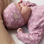 Baby iført lyserød hue med små hvide blomster og matchende heldragt